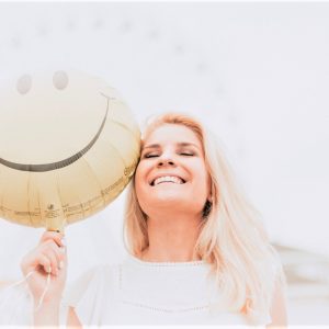 woman smiling while holding a happy face balloon